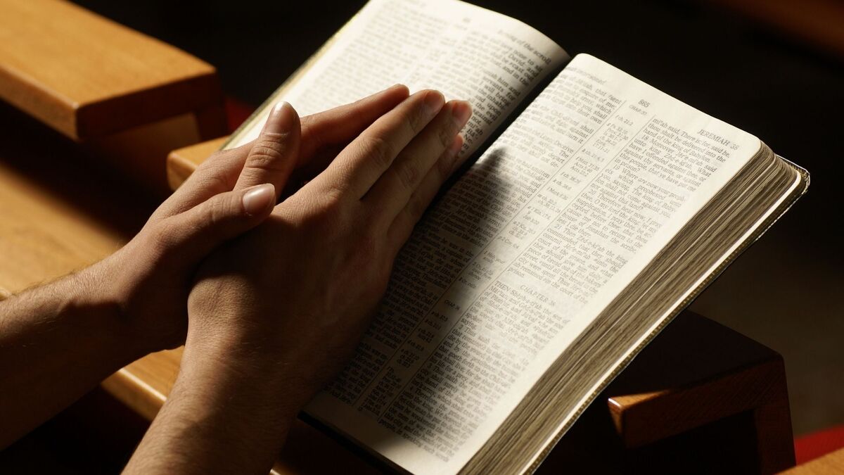 Mãos em forma de oração em cima de uma bíblia.