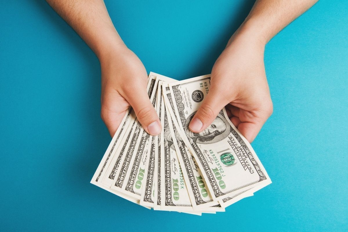 Pessoa segurando dólares em suas mãos em uma mesa azul