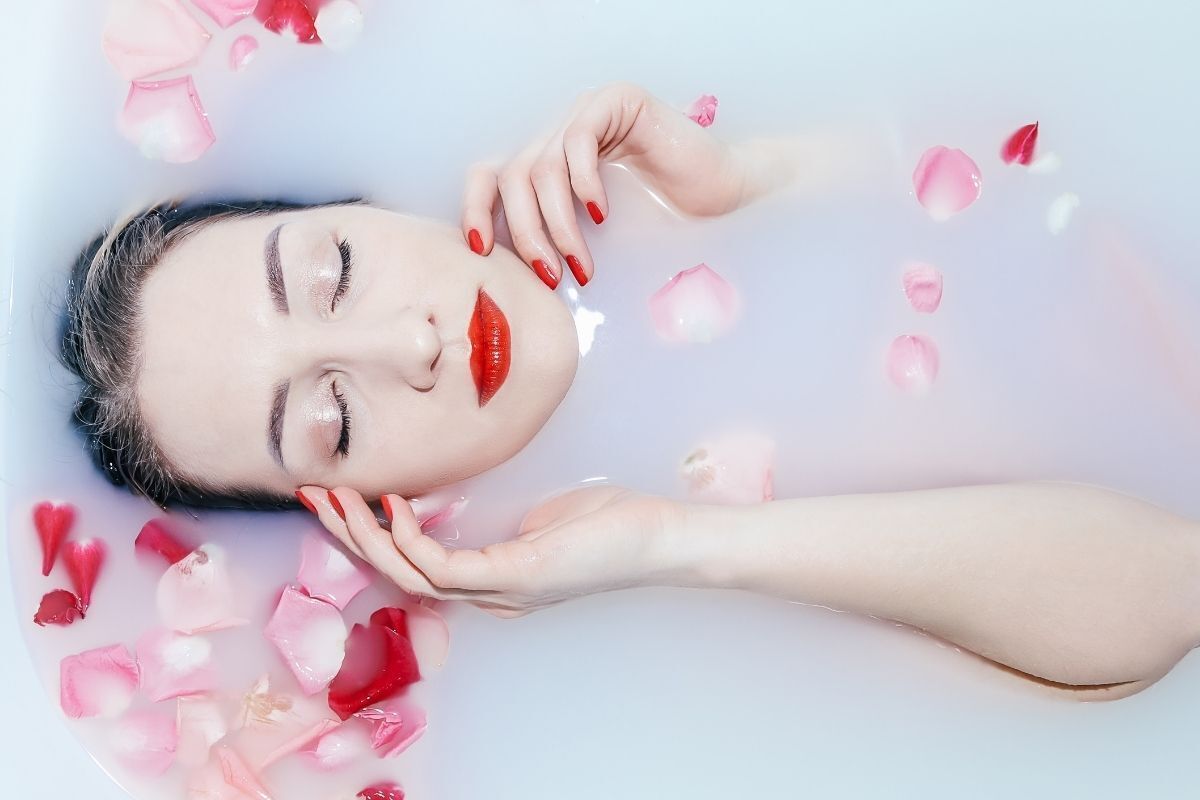 Mulher com os olhos fechados deitada em uma banheira com leite e rosas