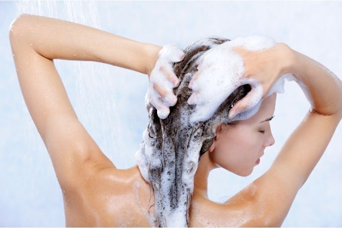 Mulher com espuma de shampoo no cabelo durante o banho