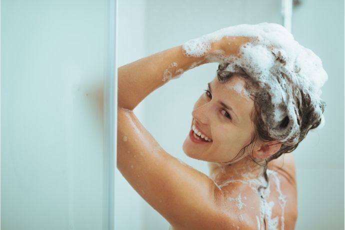 Mulher sorridente lavando o cabelo no banho com shampoo