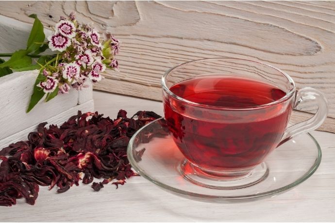 Chá de hibisco em xícara ao lado de flores secas 