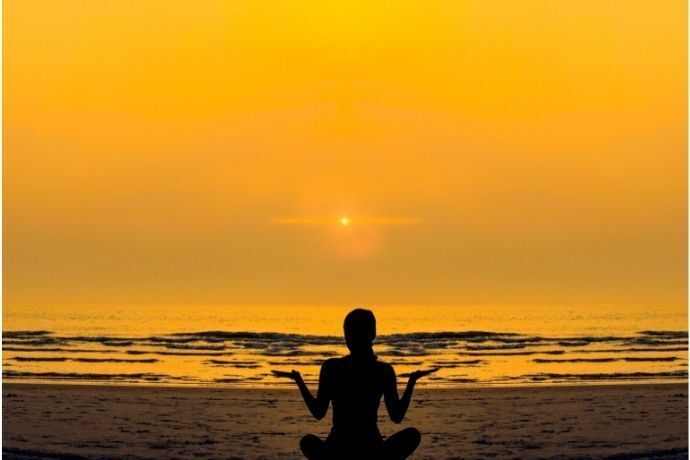 Mulher meditando na praia no nascer do sol