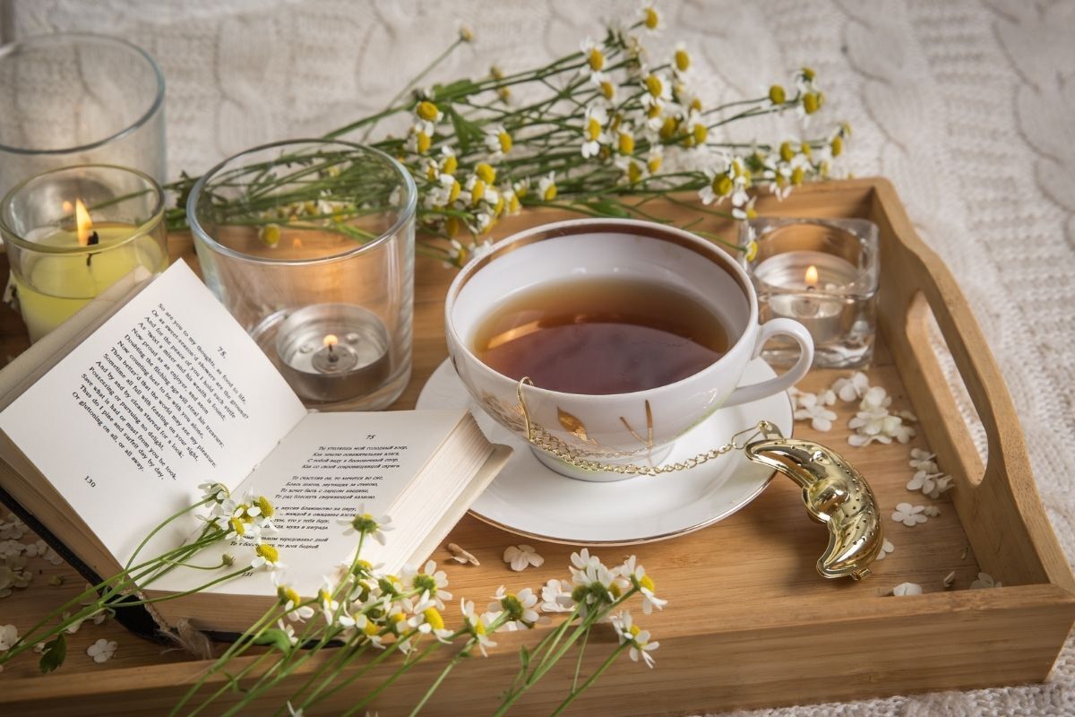 Xícara de chá ao lado de livro aberto e folhas de camomila.