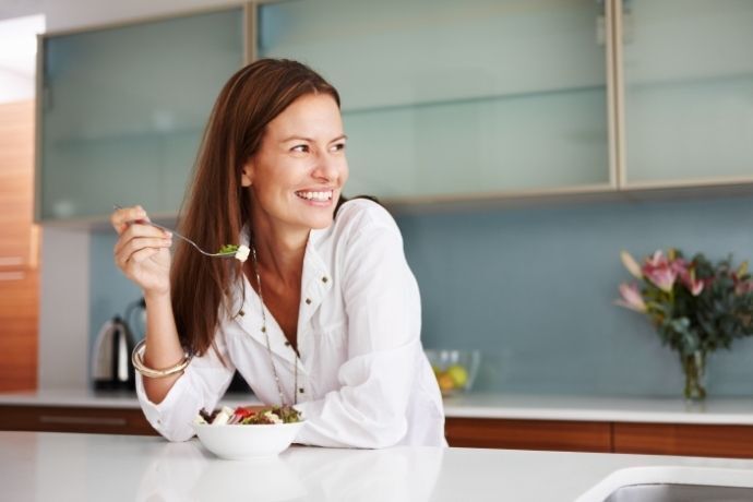 Mulher na cozinha comendo alimentos saudáveis