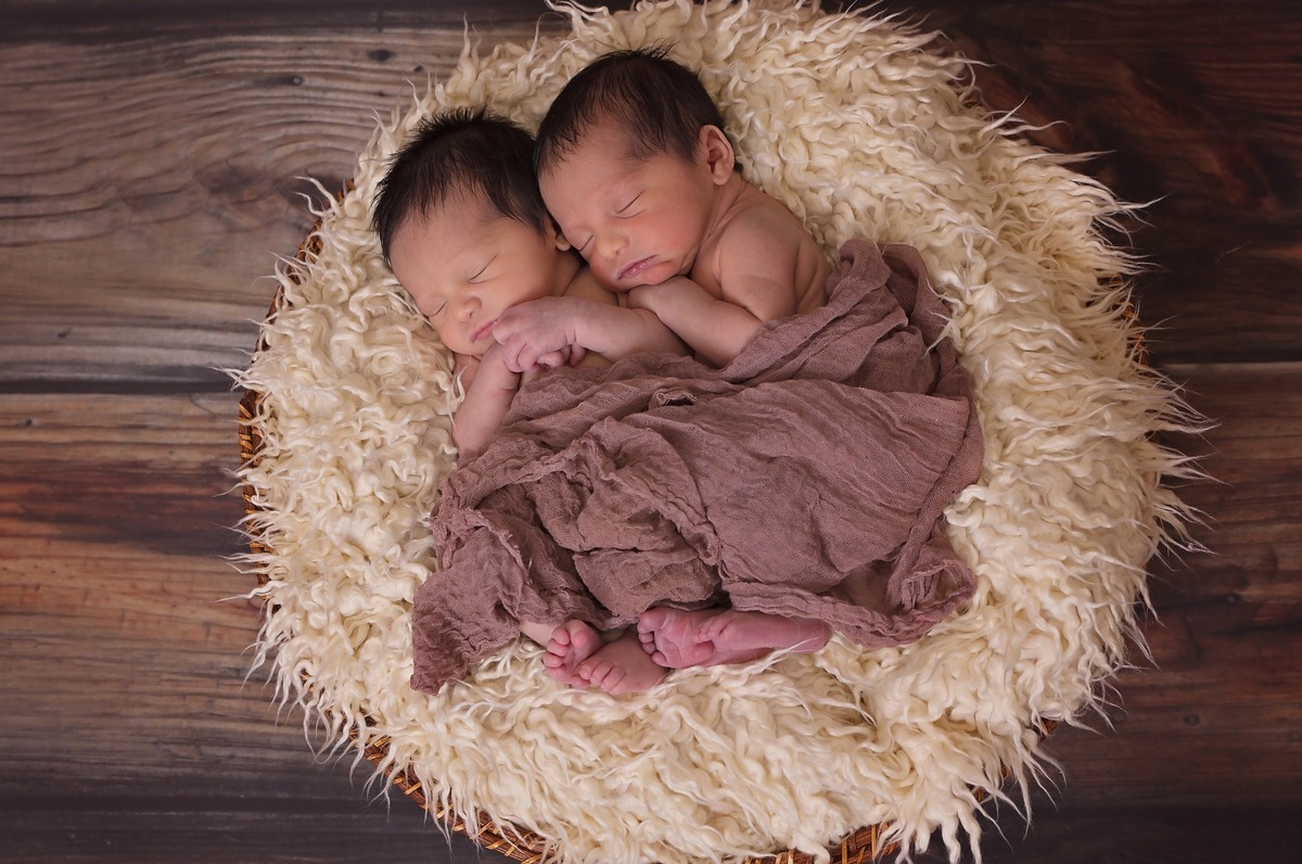 Dois bebês gêmeos dormindo dentro de cesto de palha.