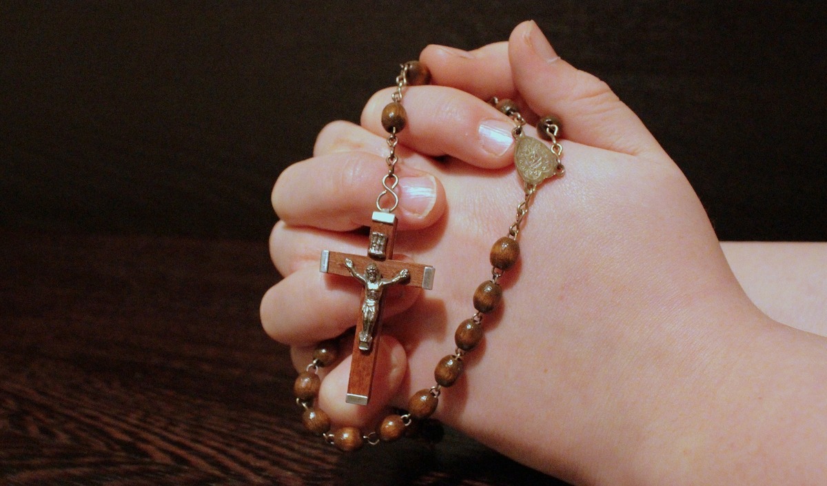 Mãos em posição de oração enquanto seguram rosário. 