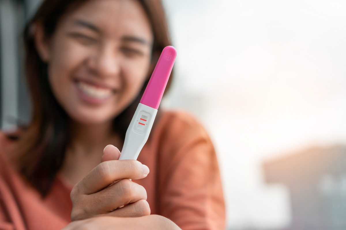 Mulher sorrindo segurando teste de gravidez positivo