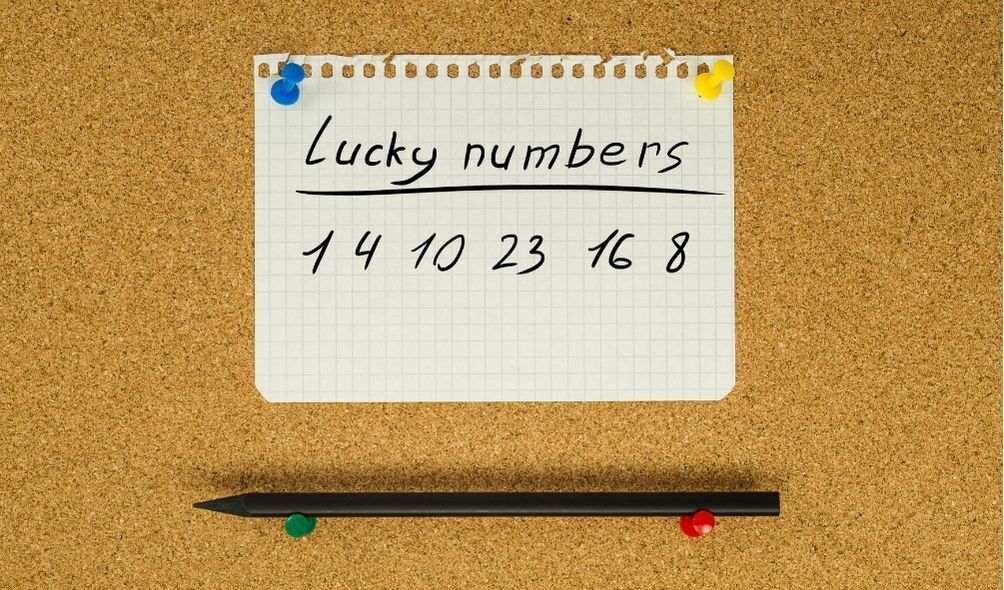Papel escrito "Lucky numbers 1, 4, 10, 23, 16, 8" pregado em um mural, com uma caneta embaixo.