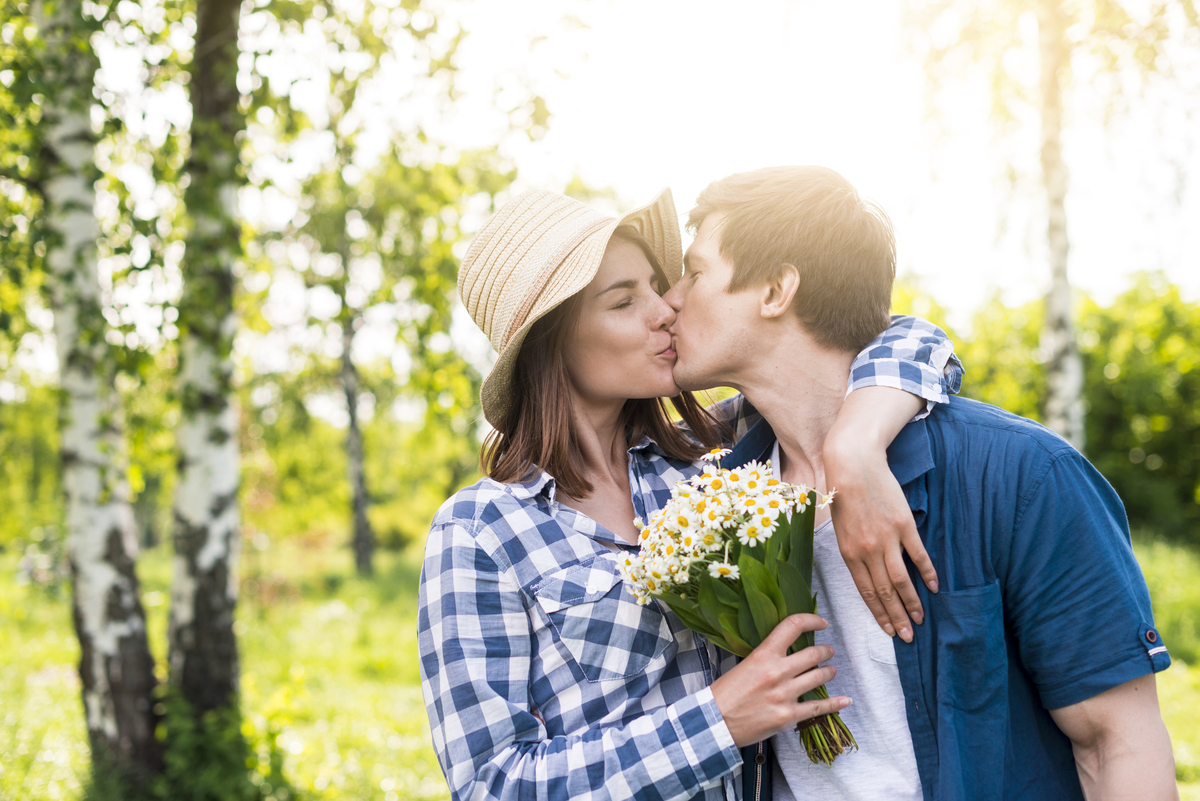 Casal se beijando com mulher segurando buquê de flores
