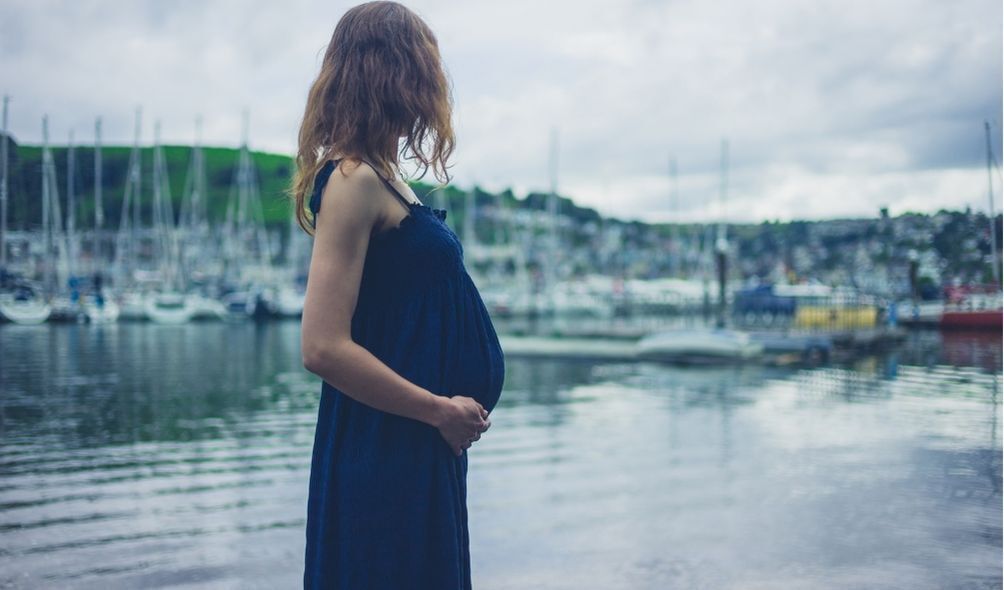 Mulher em um porto, grávida, em vestido azul