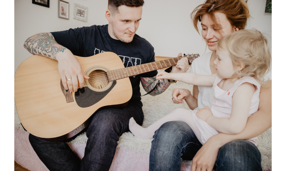 Homem tocando violão ao lado da mulher e filha.