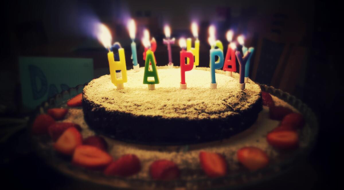 Bolo de aniversário com velas escrito "Feliz Aniversário" em inglês.