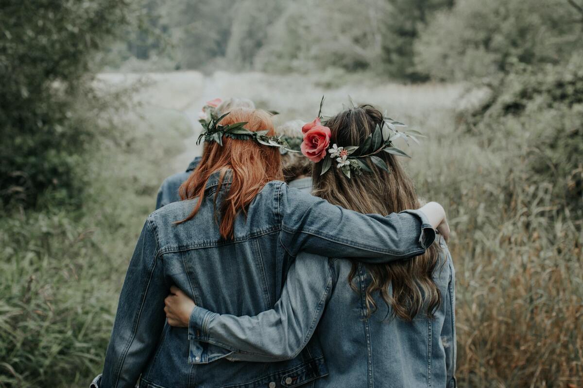 Duas mulheres usando coroas de flores e se abraçando em uma floresta.