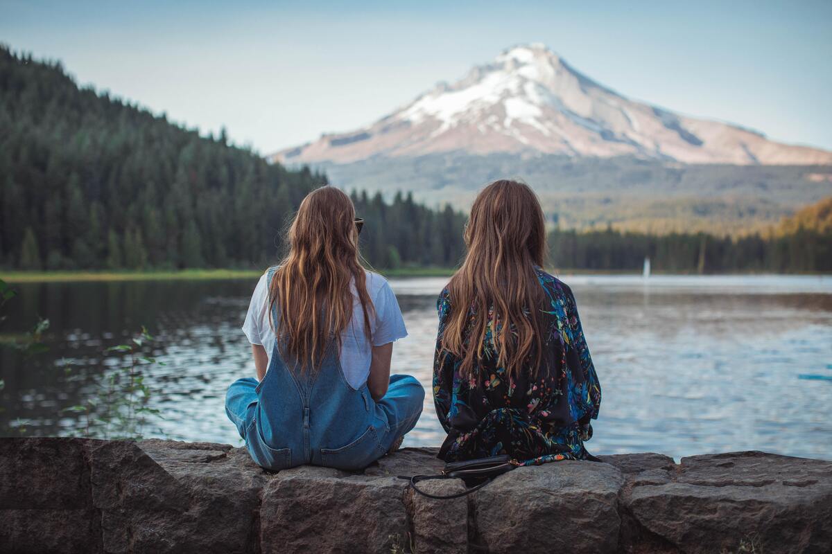 Duas mulheres sentadas de costas encarando uma paisagem natural.