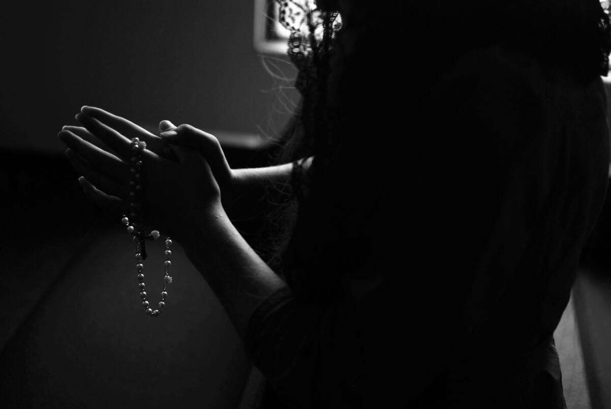 Mulher rezando com um terço na mão.