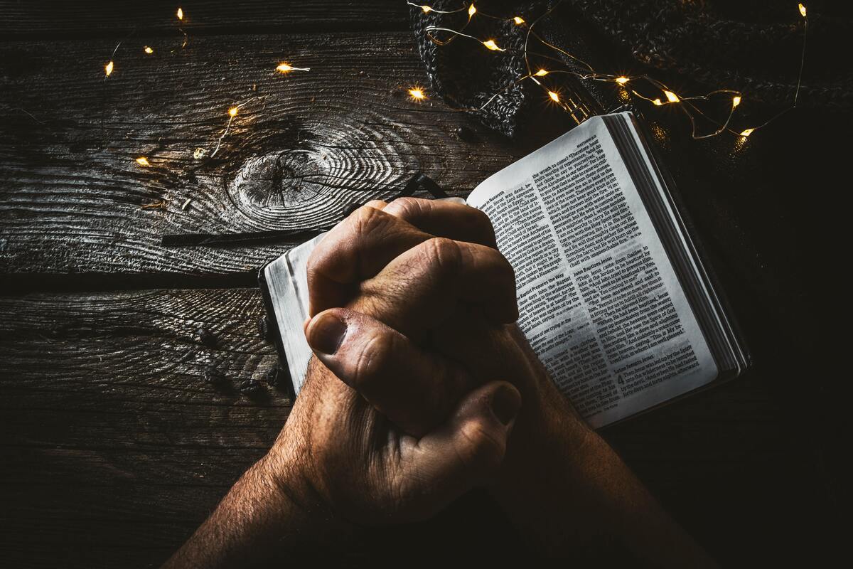 Homem rezando em cima de uma bíblia.