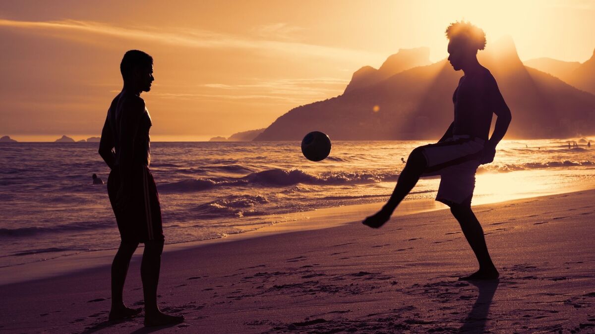 Duas pessoas jogando bola na praia.