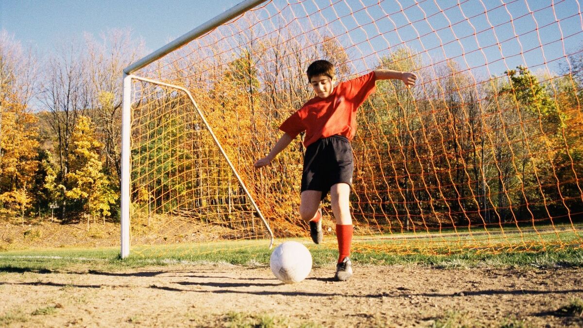 Criança chutando uma bola em um campo.
