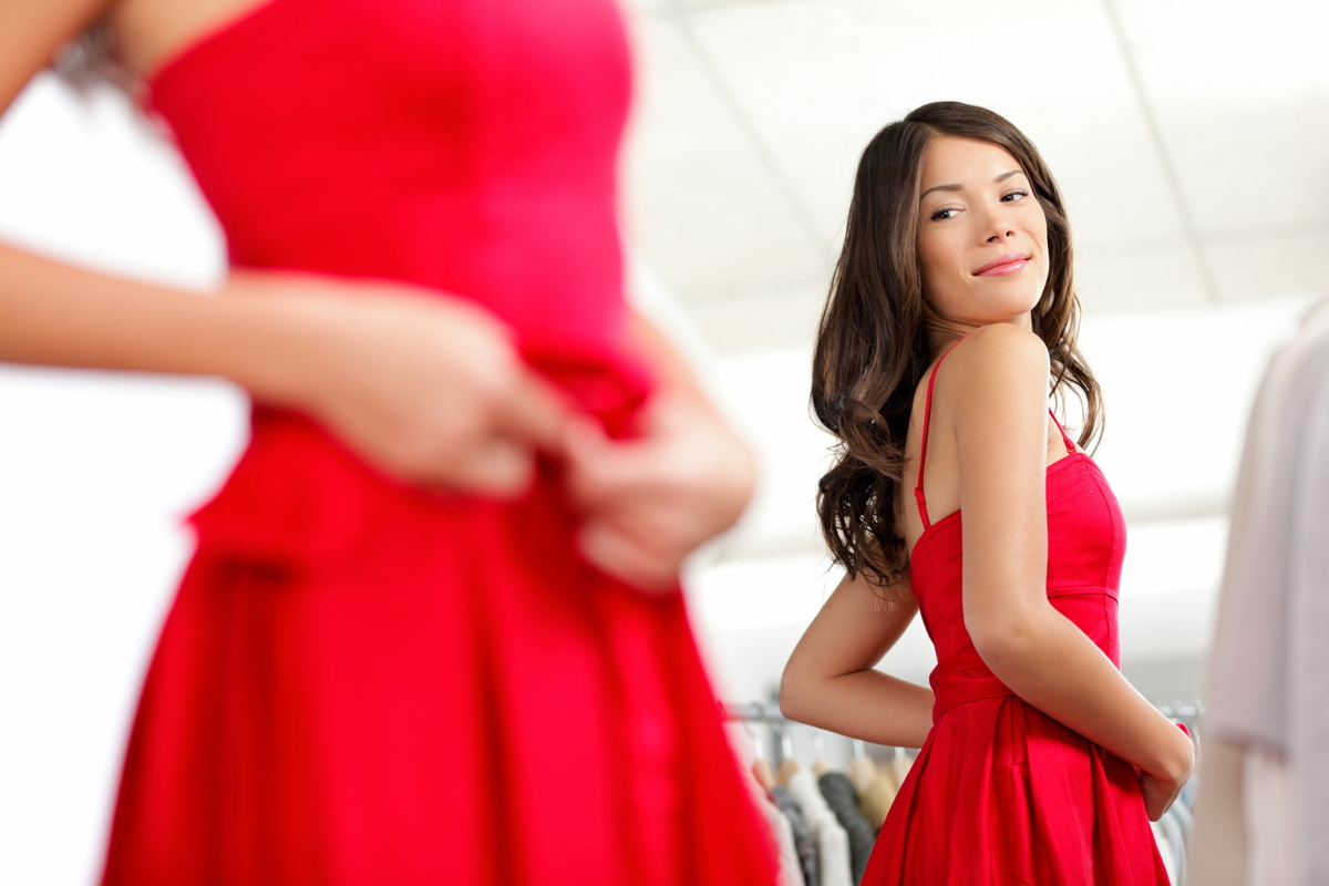 Mulher provando vestido vermelho diante de espelho.