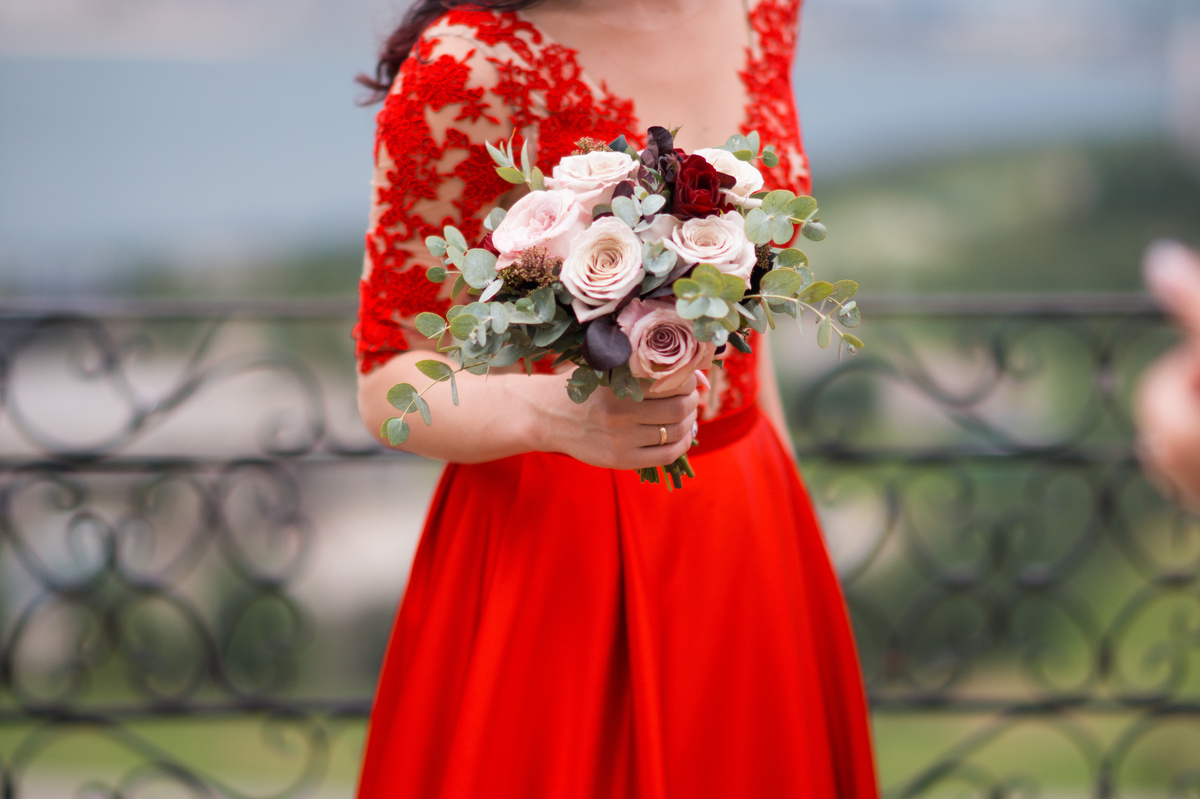 Mulher usando vestido vermelho de renda, enquanto segura buquê de flores.