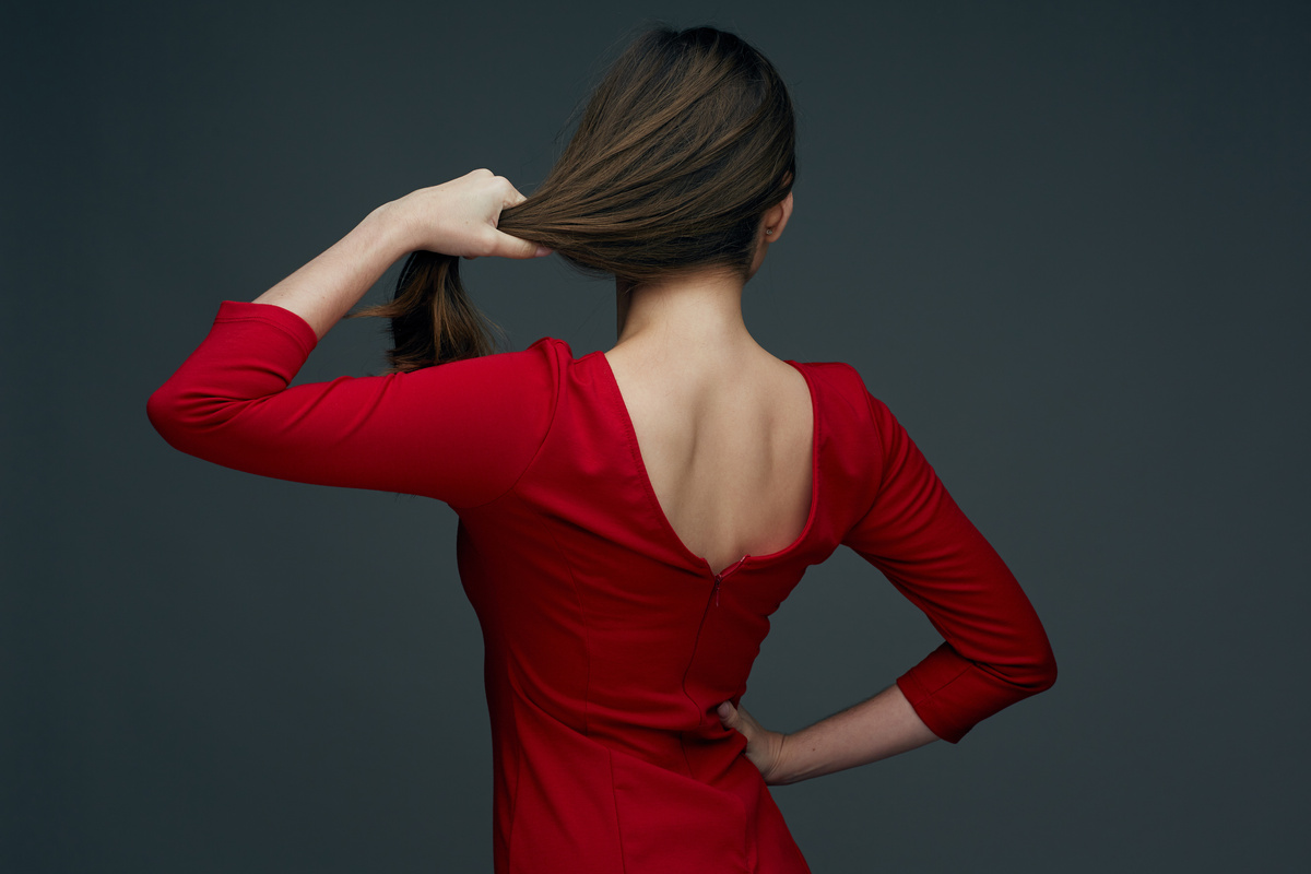 Mulher de costas segurando seu cabelo, enquanto usa um vestido vermelho.