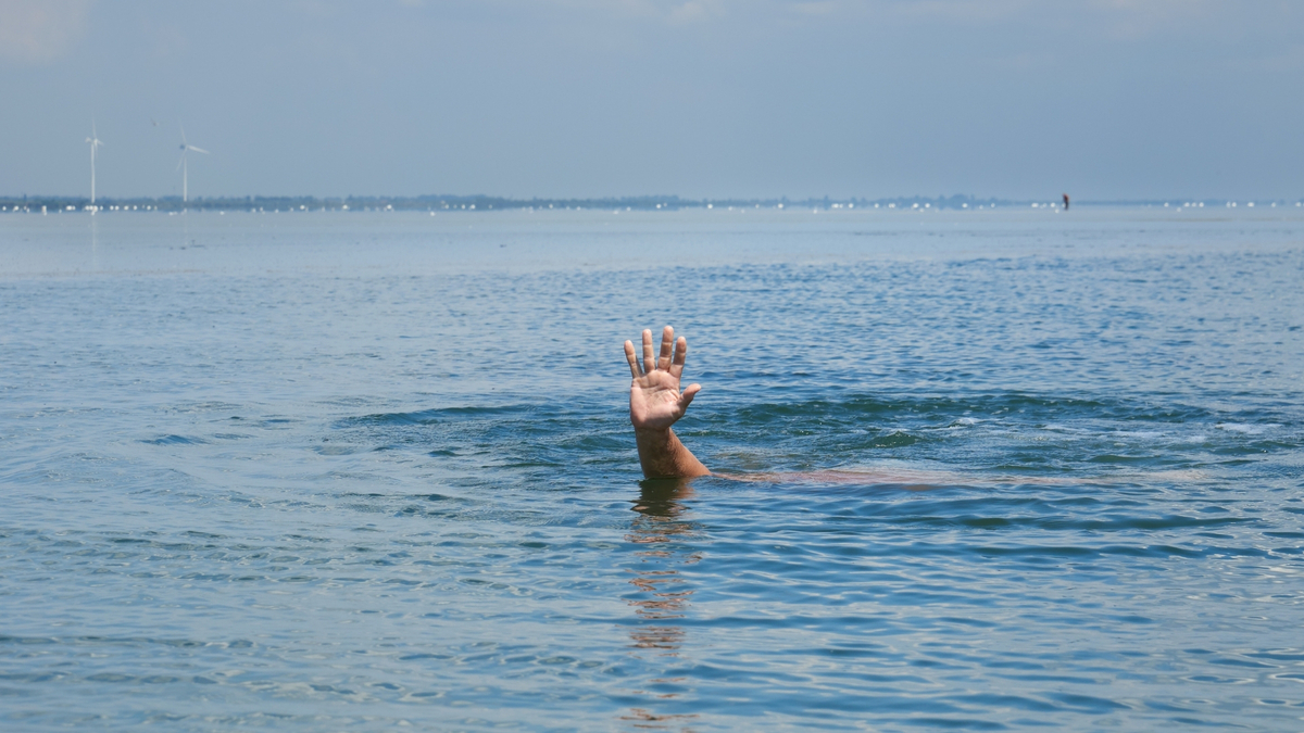 Pessoa na água com a mão pra cima.