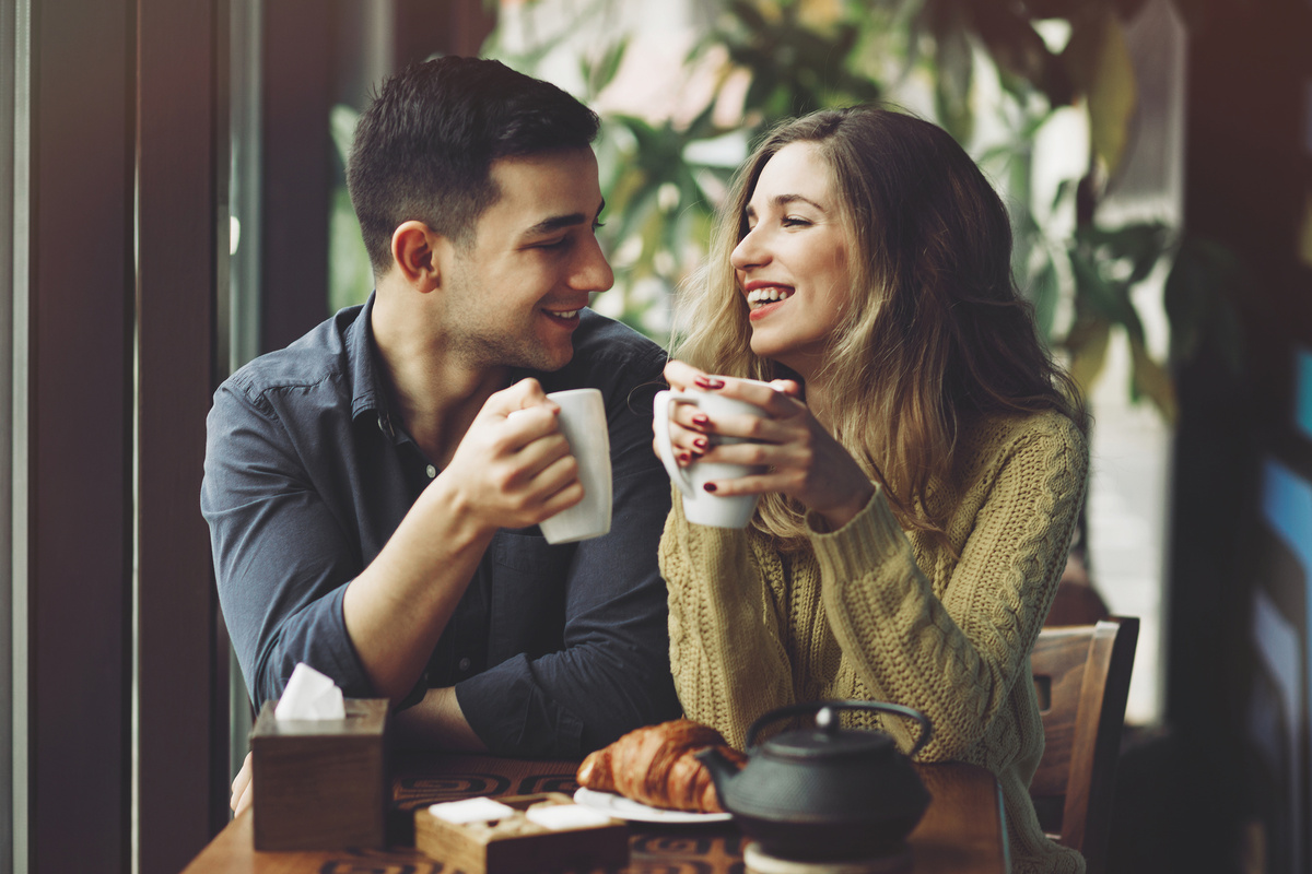 A imagem mostra um casal conversando em uma cafeteria, simbolizando a relação entre Libra e Sagitário que é de muita conversa.