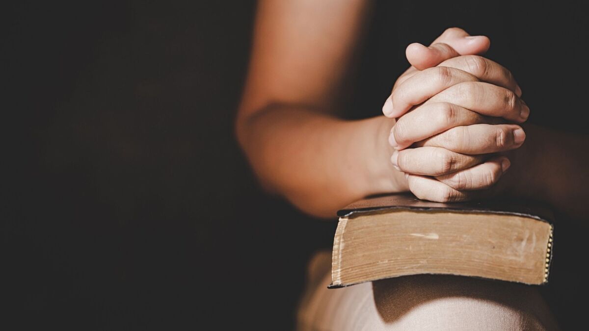 Mão em sinal de oração em cima de uma bíblia.
