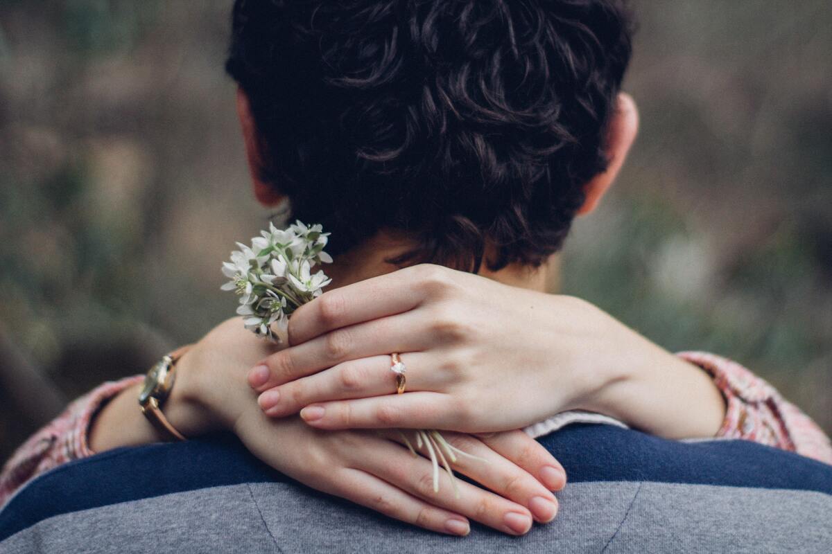Mãos femininas segurando uma flor ao redor do pescoço de um homem.