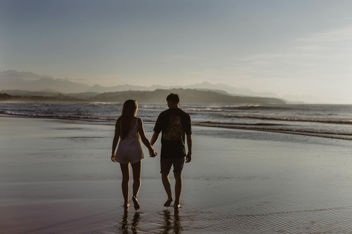Casal andando de mãos dadas na praia.
