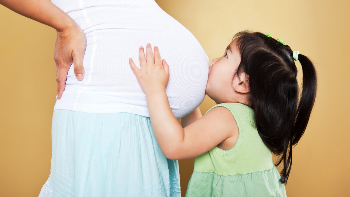 Menina beijando a barriga de uma mulher grávida.