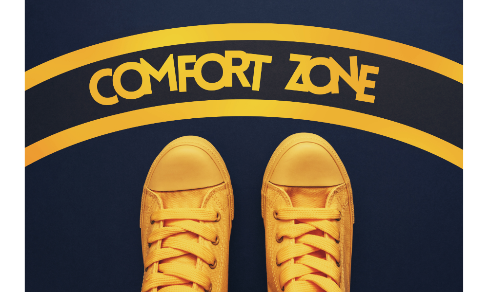 Pés com tênis amarelo ao lado de linhas e um escrito no chão com "Comfort zone" - Zona de conforto.