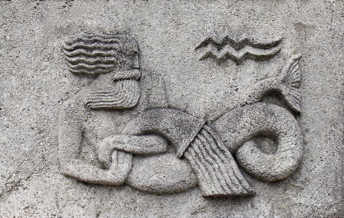Pedra esculpida com homem despejando água de jarro, simbolizando o signo de Aquário. 