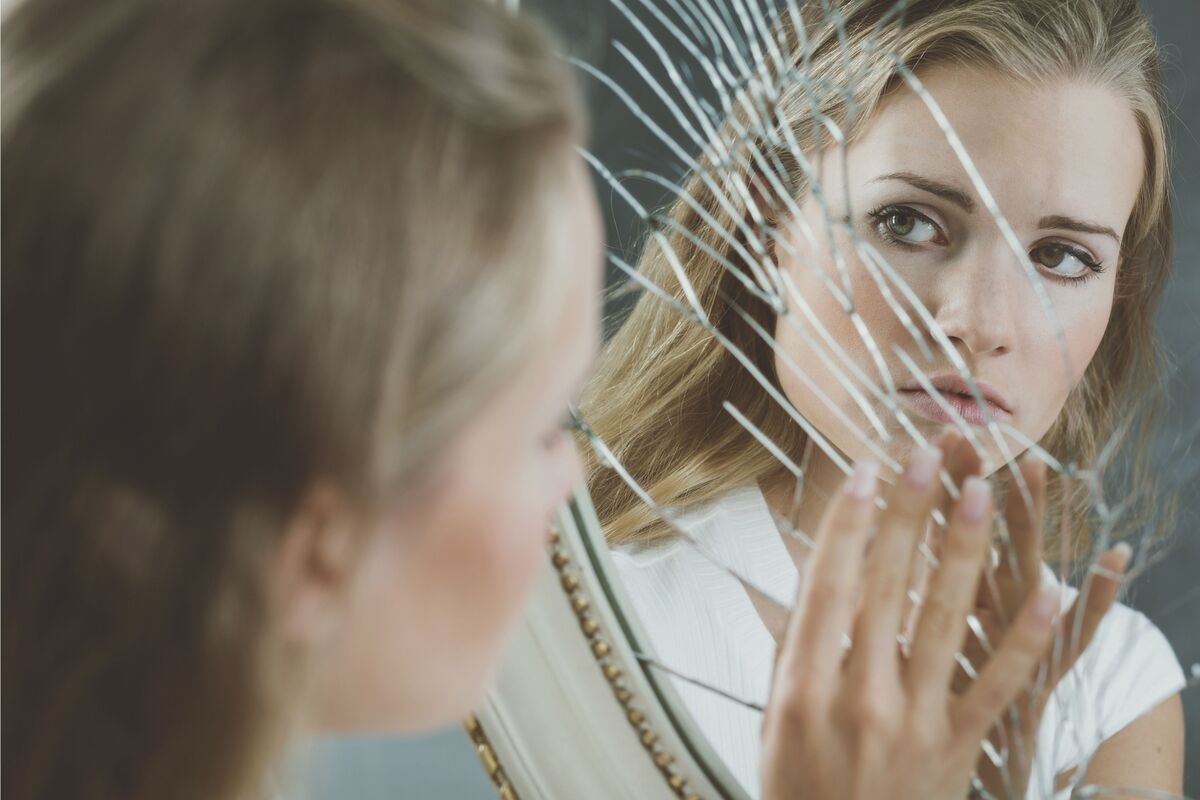 Mulher observando espelho quebrado.