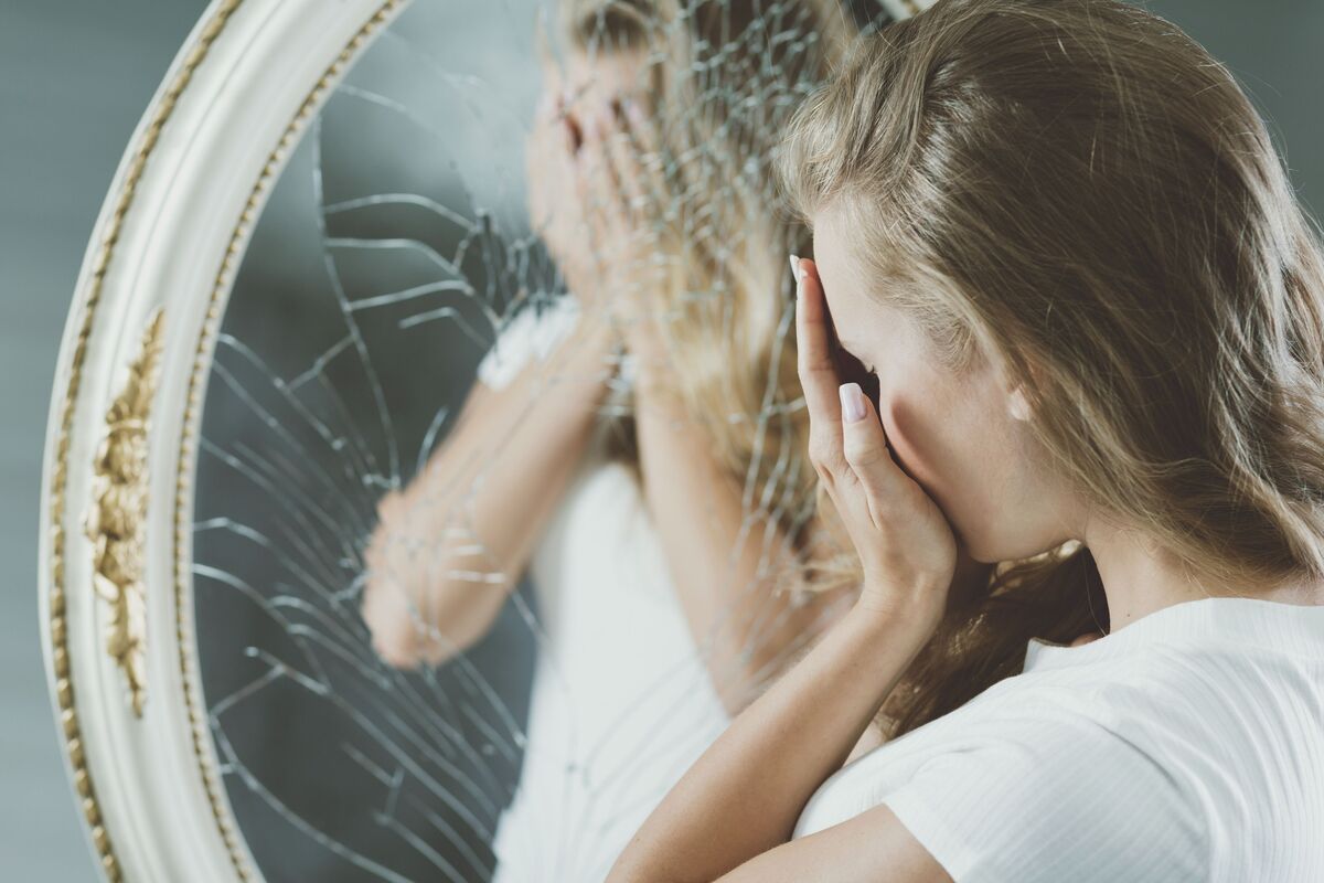 Mulher em frente a espelho quebrado.