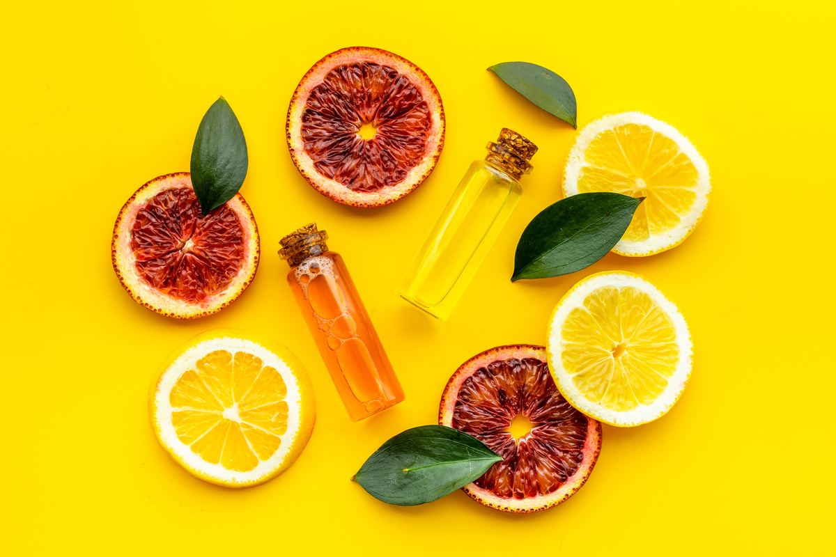 Conta-gotas com óleo essencial de laranja e rodelas de laranja em fundo amarelo