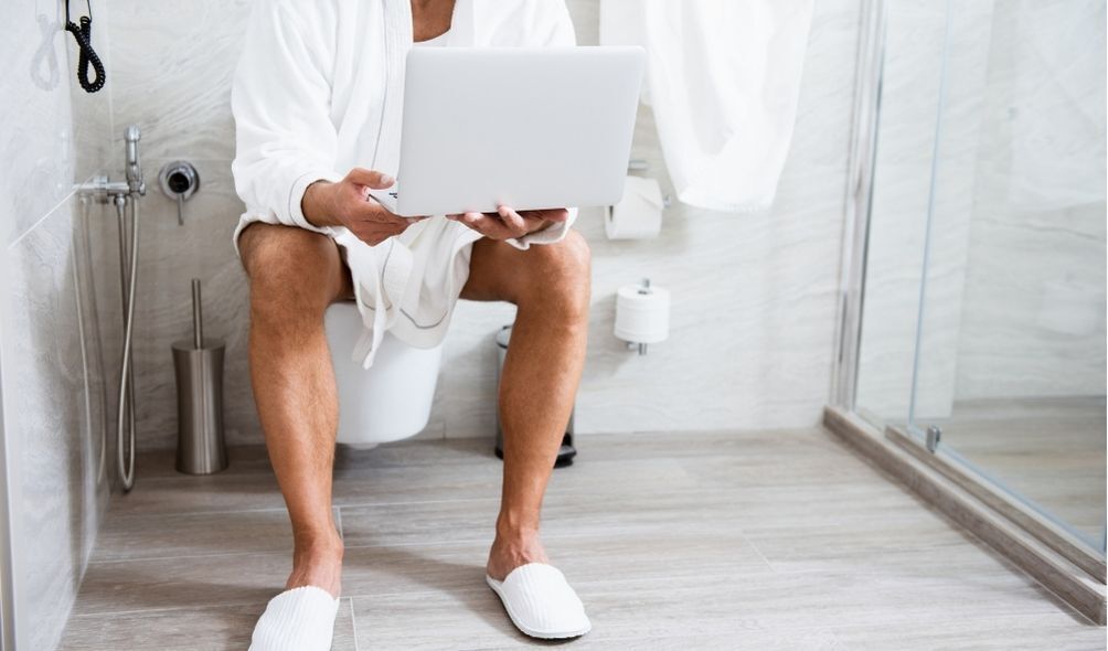 Imagem de homem sentado no vaso sanitário segurando laptop