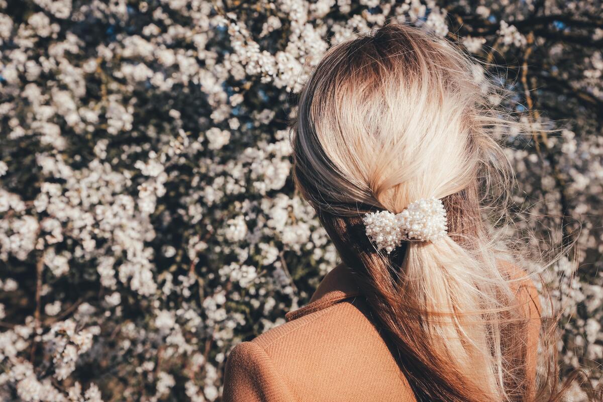 Mulher com cabelo loiro de costas, flores ao fundo.