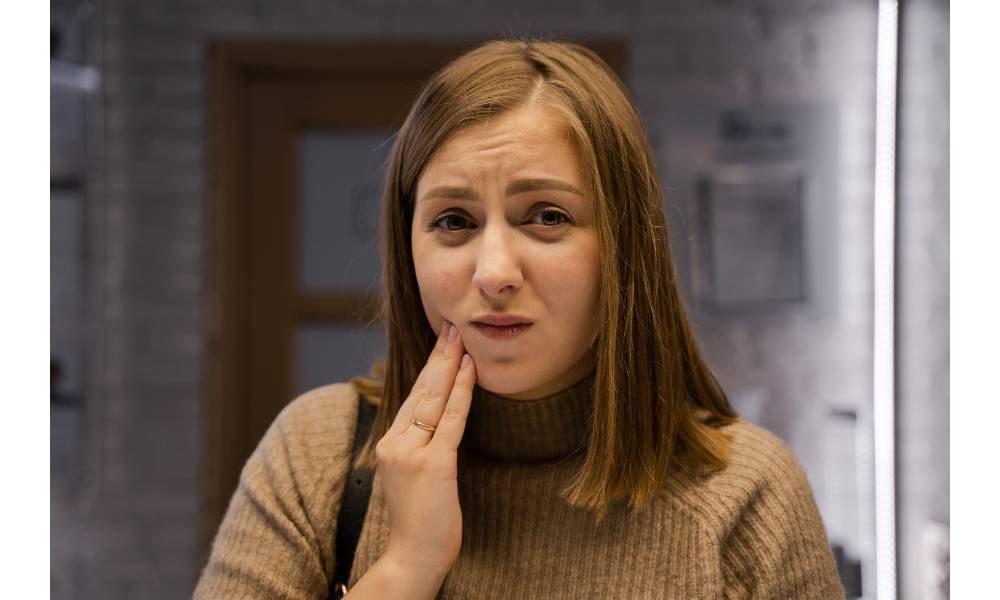 Mulher com dor de dente colocando a mão sobre o rosto.