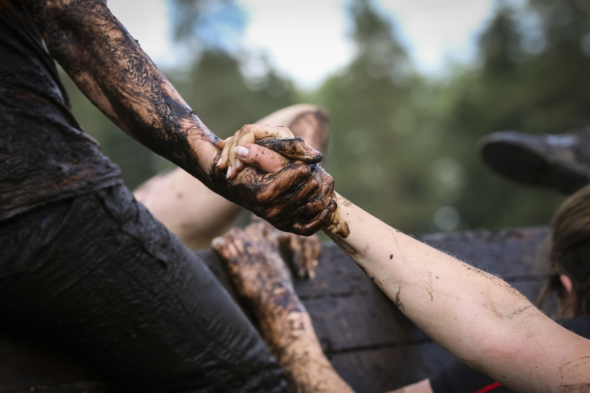 Uma pessoa dando a mão para outra, enquanto ambas estão cobertas de lama preta.