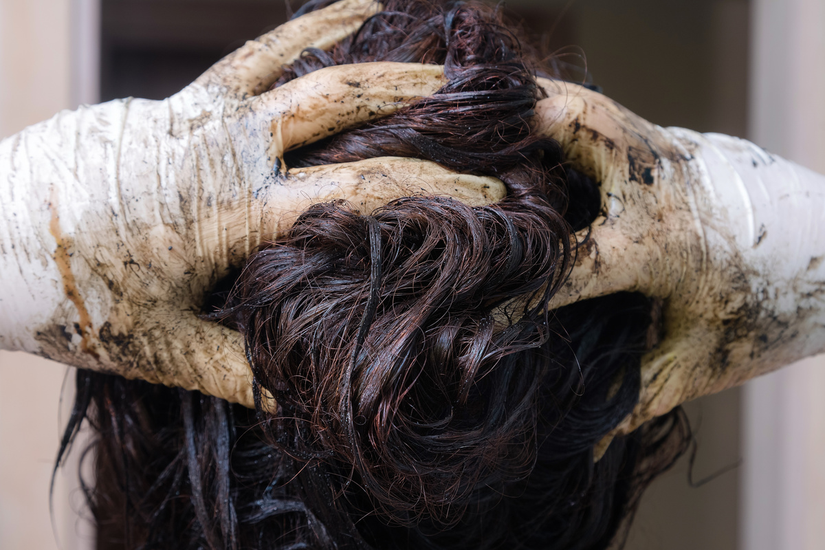 Mãos com luvas esfregando tinta em couro cabeludo, enquanto pinta o cabelo. 