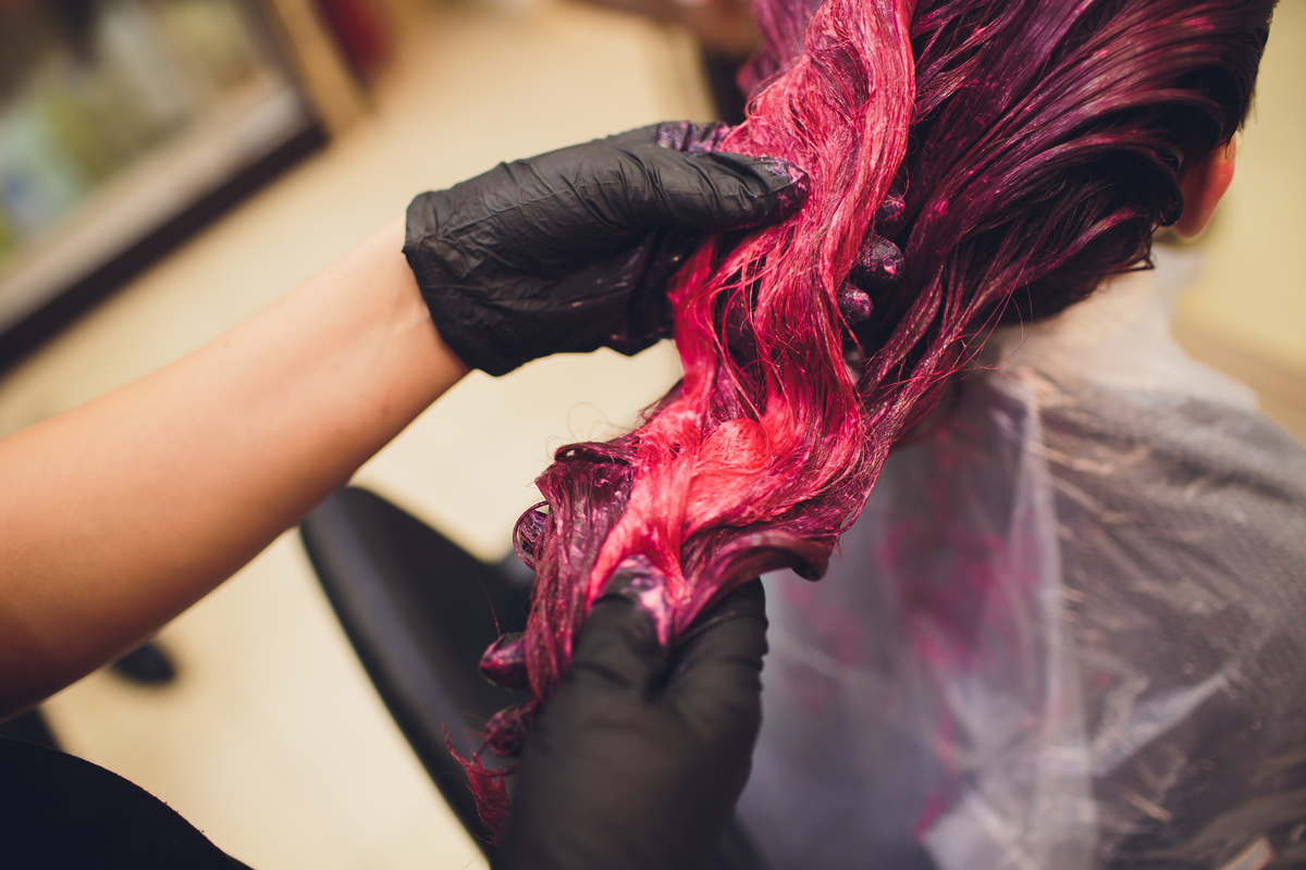 Pessoa pintando o cabelo de outra de rosa. 