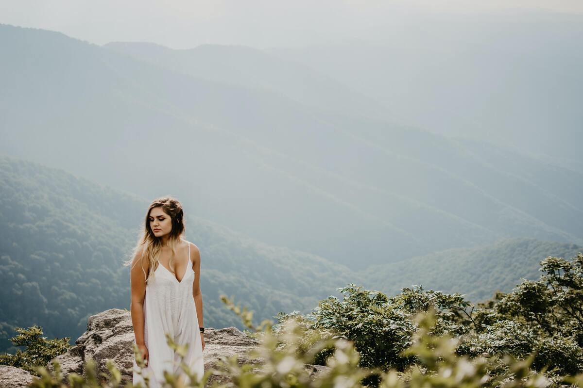 Menina usando vestido branco no topo de uma montanha.