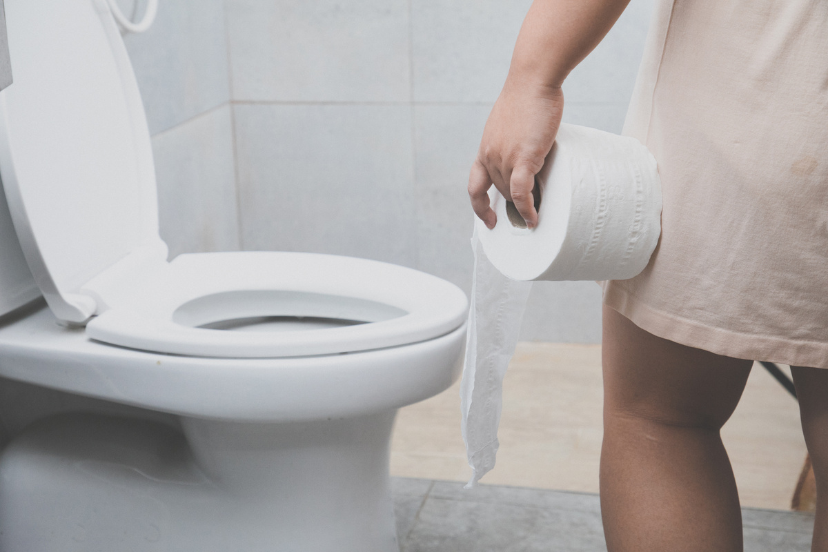 Mulher segurando papel higiênico e olhando para o  vaso sanitário