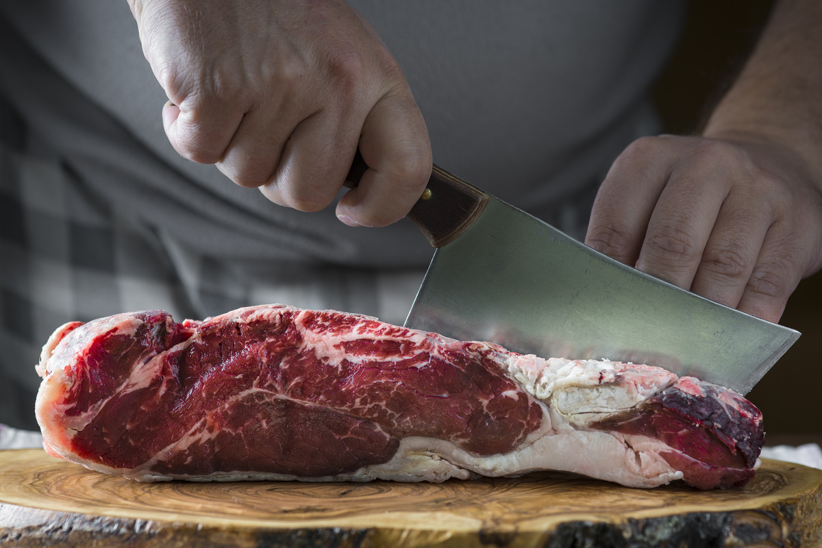 Homem cortando pedaço de carne vermelha