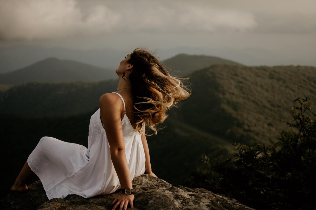 Mulher sentada em cima de uma pedra, no topo de uma montanha. 