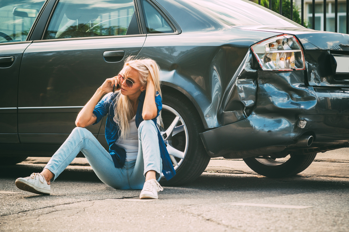 Mulher sentada do lado de um carro após o acidente.