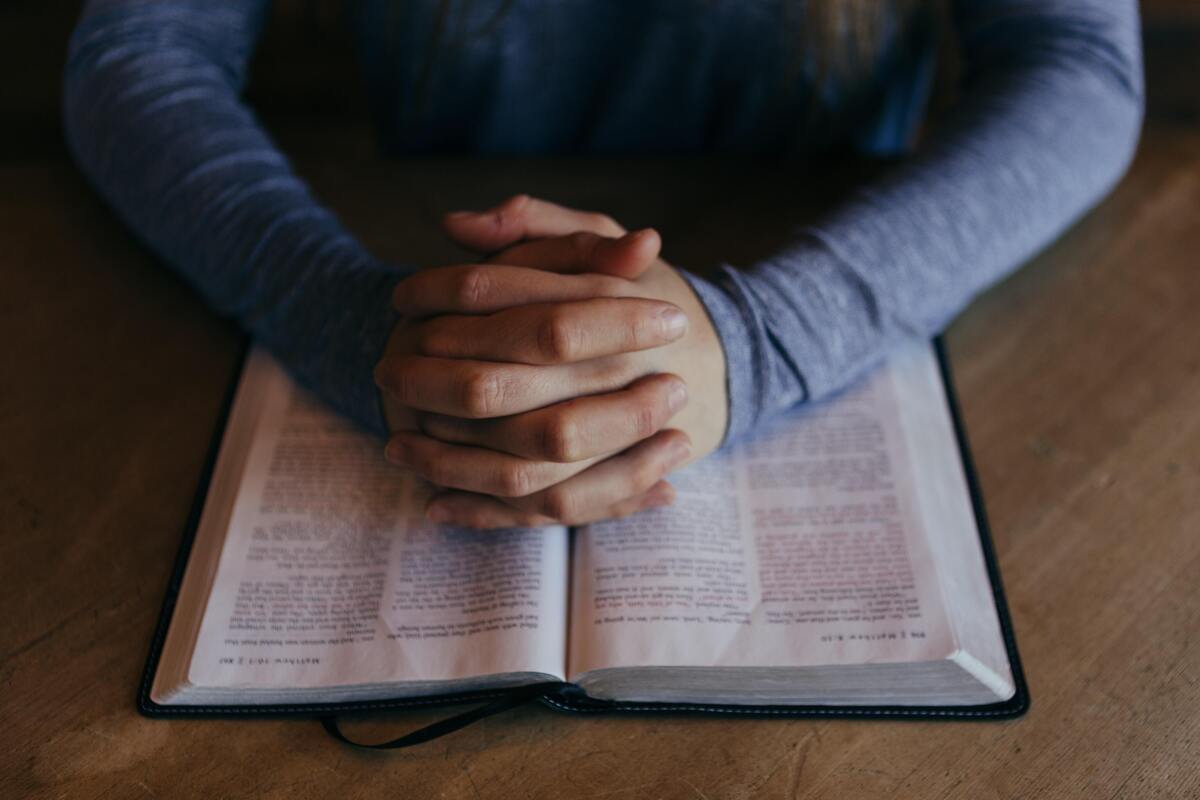 Mulher com as mãos cruzadas em cima de uma Bíblia. 