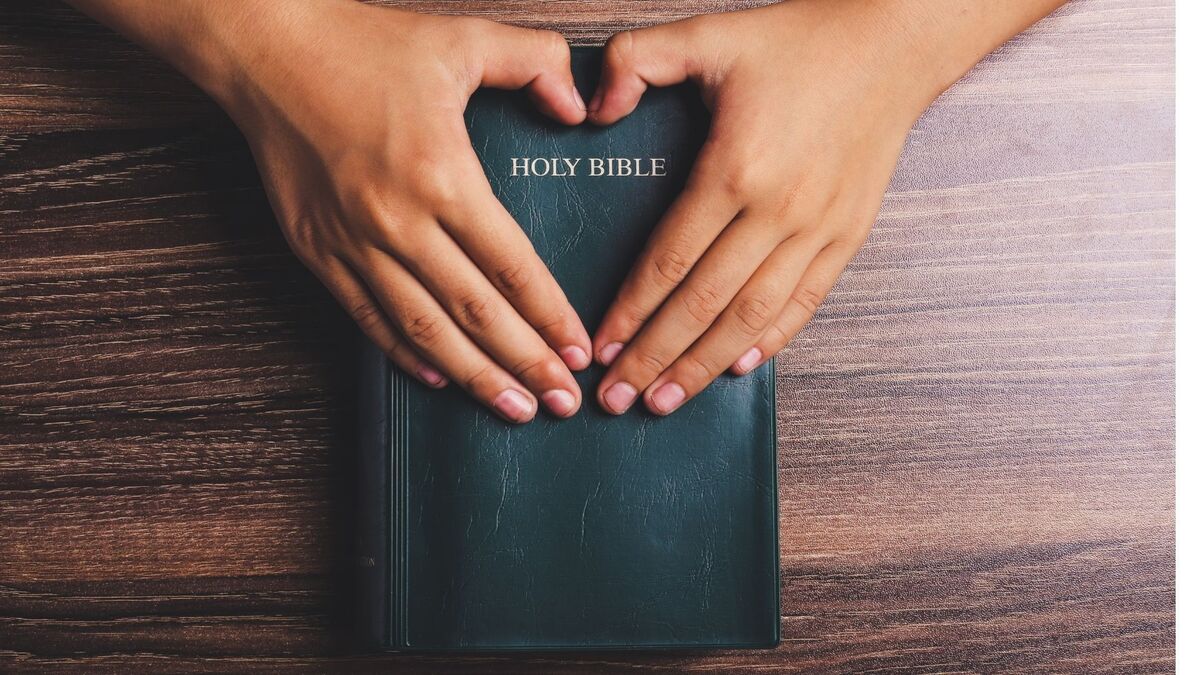 Mãos dobradas em forma de coração com uma bíblia.